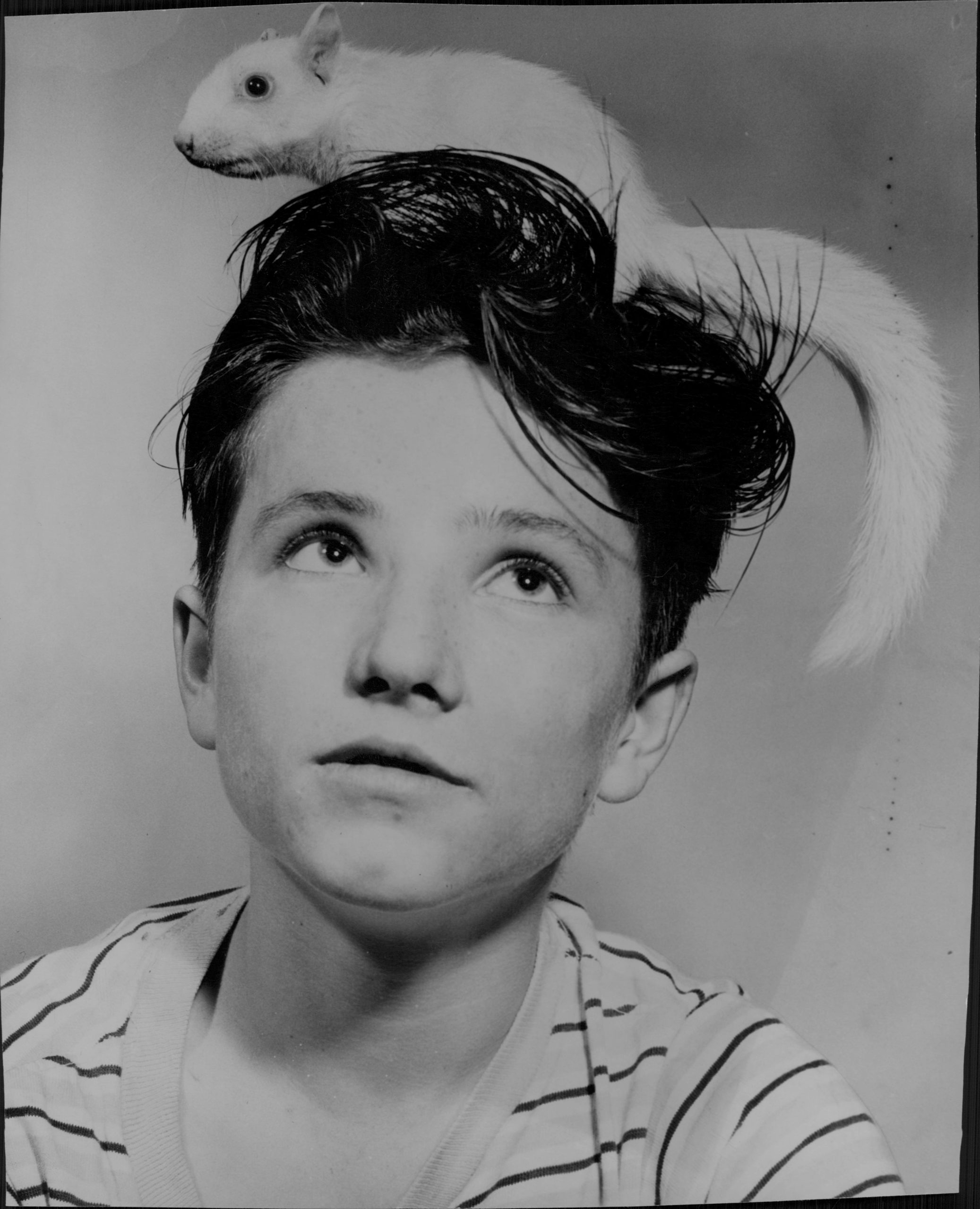 Black and white photo of a boy with an albino squirrel on his head.