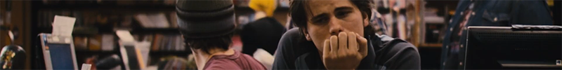 A man sitting at a video store counter, resting his chin on his hand.