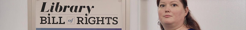 A woman stand next to a sign reading "The Library Bill of Rights."